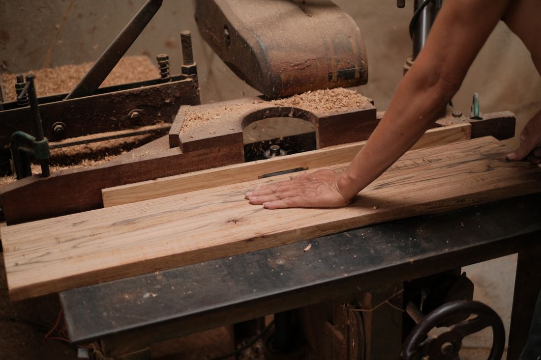 A carpenter guiding a wooden board through a planer in a workshop